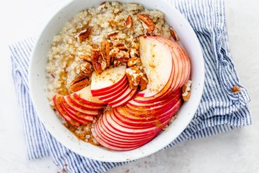 Apples with pecans, cinnamon and maple syrup top oatmeal-style quinoa served in a white bowl.