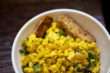 A golden tofu scramble in a white bowl with two pieces of tempeh bacon