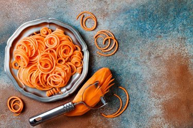 Sweet potato noodles on a silver dish, with a spiralizer on a colorful background.