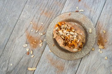 Baked sweet potato with almonds and cinnamon on a plate, on a wooden background.