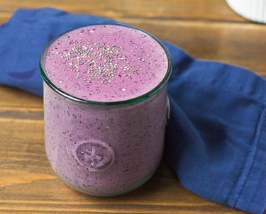 A purple smoothie in a clear glass topped with chia seeds