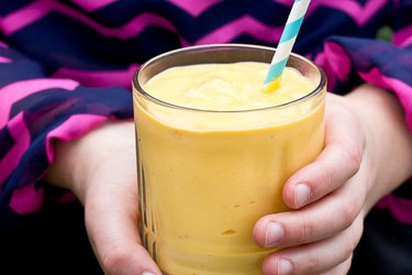 Sweet potato smoothie in a glass being held by a woman's hands.