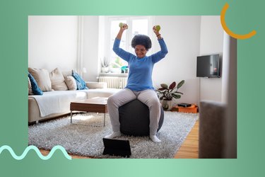 adult wearing a long sleeve blue shirt and gray leggings doing an overhead press exercise with light dumbbells on a black stability ball in front of a laptop as part of a 4 week arms challenge