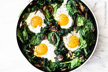 A pan holds a bed of cooked spinach and mushrooms, topped with four baked eggs