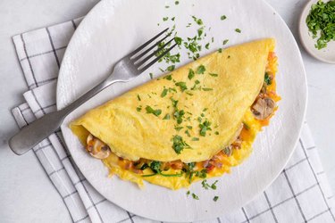 A golden omelet folded over a host of chopped veggies atop a white plate