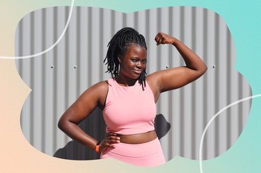 a person wearing a matching light pink tank top and leggings is flexing their biceps outside in front of a gray wall on a sunny day