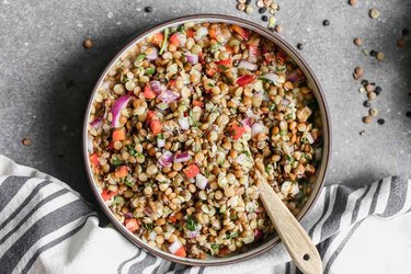 Lentil Salad in a gray bowl with wooden spoon and striped napkin
