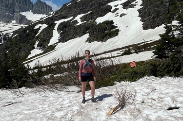 the author stands in a snowfield in front of a glacier in Glacier National Park wearing Bombas quarter hiking socks