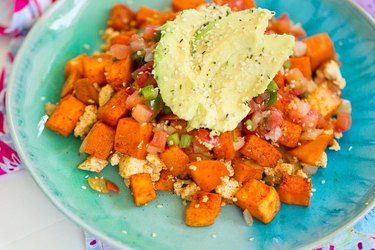 Sweet potato protein hash with avocado and hemp seeds on a turquoise plate.