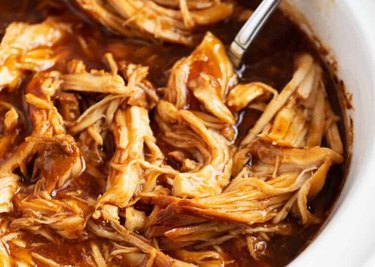 Saucy slow cooker barbecue chicken shredded in a white dish.