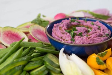 Purple sweet potato hummus in a blue bowl with vegetables.