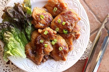 3-Ingredient Apple Juice Chicken thighs topped with green onions and served with lettuce leaves on a white plate.