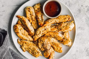 Instant pot chicken tenders with spices on top served with barbecue sauce on a white plate over gray background.