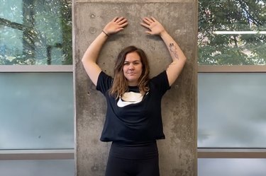 woman wearing black doing a wall angel scapular exercise against a concrete wall with windows