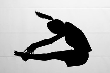 silhouette of a woman doing a pike jump exercise against a while background