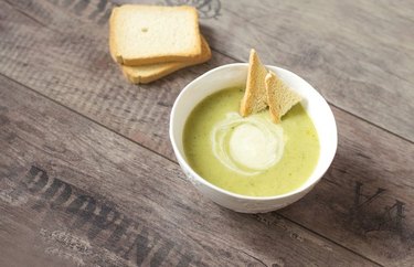 Creamy Broccoli and Cauliflower Soup in a white bowl with slices of toast over wooden background.