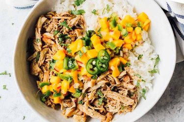 White bowl with shredded jerk chicken alongside white rice topped with spicy mango salsa.