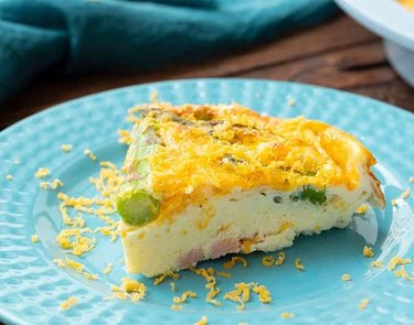 A slice of Ham and Asparagus Crustless Quiche on a bright blue plate