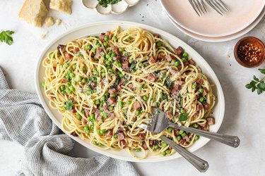 An overhead photo of a big white bowl of Pasta with Ham and Peas on a white tablecloth