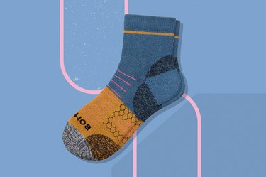 a blue, orange and gray Bombas quarter hiking sock on a blue background