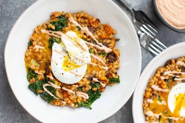 Bowl of farro mixed with greens and mushrooms topped with a poached egg and a drizzle of harissa yogurt sauce.