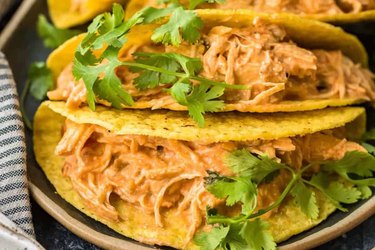 Hard corn taco shells filled with shredded creamy salsa chicken topped with cilantro leaves.