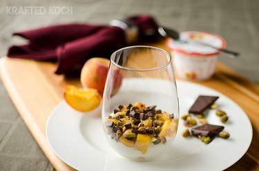 Peach Yogurt Parfait With Pistachios and Dark Chocolate in glass on plate