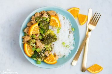 Instant Pot Orange Chicken and Broccoli on a ble plate next to cutlery on marble countertop.