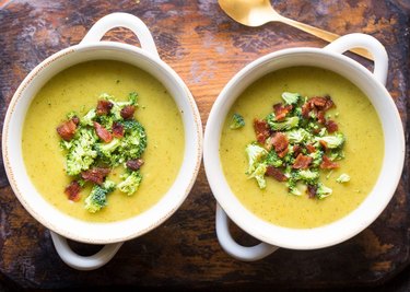 Instant Pot Broccoli Potato Soup topped with bacon in two white bowls on wooden tabletop.
