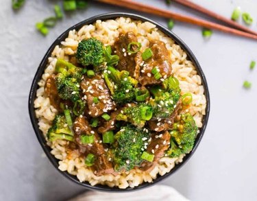 Instant Pot Beef and Broccoli over brown rice topped with chopped scallions in a black bowl over white countertop.