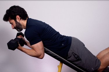 closeup of a caucasian man doing an incline spider curl exercise with dumbbells against a white background