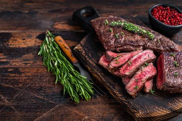 Marinated beef tenderloin with fresh thyme garnish on a wooden cutting board on wooden table