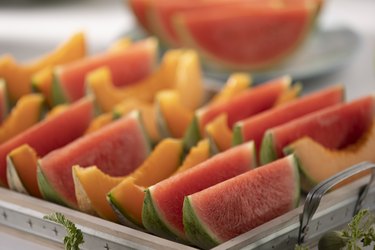 slices of watermelon and cantaloupe on a silver catering platter with handles