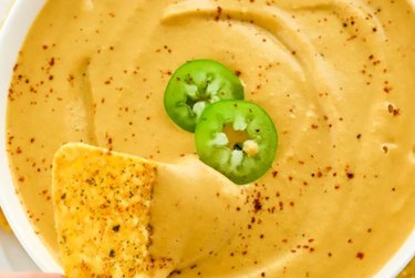 Creamy Vegan Queso with a tortilla chip and jalapeno slices