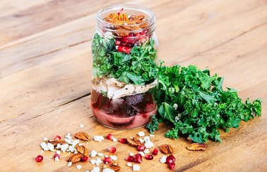 Mason jar salad with chicken, kale and beetroot on a wooden table.