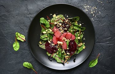 Beet, Grapefruit, Walnut Salad With Mint Dressing on a black plate on charcoal tabletop.