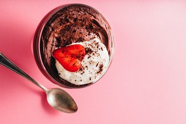 Vegan Chocolate Protein Pudding topped with whipped cream and a slices strawberry over pink background.