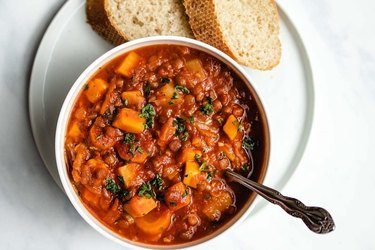 Instant Pot Lentil Soup in a white bowl with sliced white bread over marble countertop.