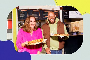 a man and a woman smile while holding pizzas