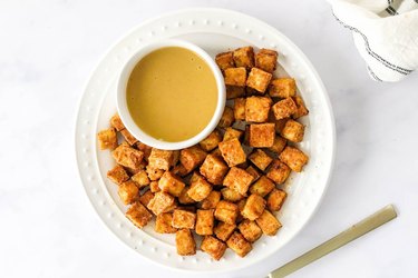 air fryer crispy tofu cubes on a white plate with mustard on the side on marble countertop