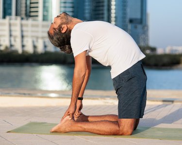 person doing yoga on pier in Abu Dhabi, kneeling and bending over backwards touching heels, Camel pose, Ushtrasana, sea and cityscape in the background