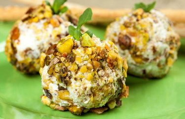 Pistachio-crusted cheese ball with crackers on greem. tablecloth