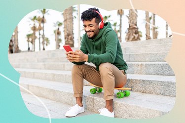 a man with headphones sitting on steps smiles at his phone