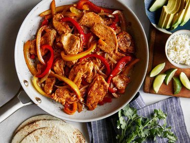 Chicken Fajitas in gray bowl on marble table with avocado and lime wedges
