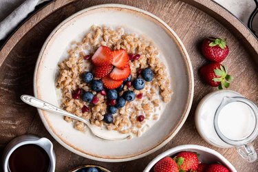 Bowl of farro with milk topped with berries in a bowl on wooden table.