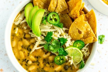 Close up of white bean chili topped with avocado tortilla chips cilantro and cheese