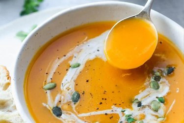 Close up of butternut squash soup in a white bowl with a silver spoon