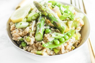 Spring Vegetable Instant Pot Brown Rice Risotto in a white bowl topped with sliced asparagus and snow peas.