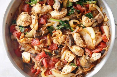 One-Pan Eggplant Chicken Dinner with spinach and tomatoes in a white bowl.