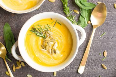 Instant Pot Pumpkin Butternut Squash Bisque with pumpkin seeds and thyme in a bowl next to golden spoon on gray countertop.